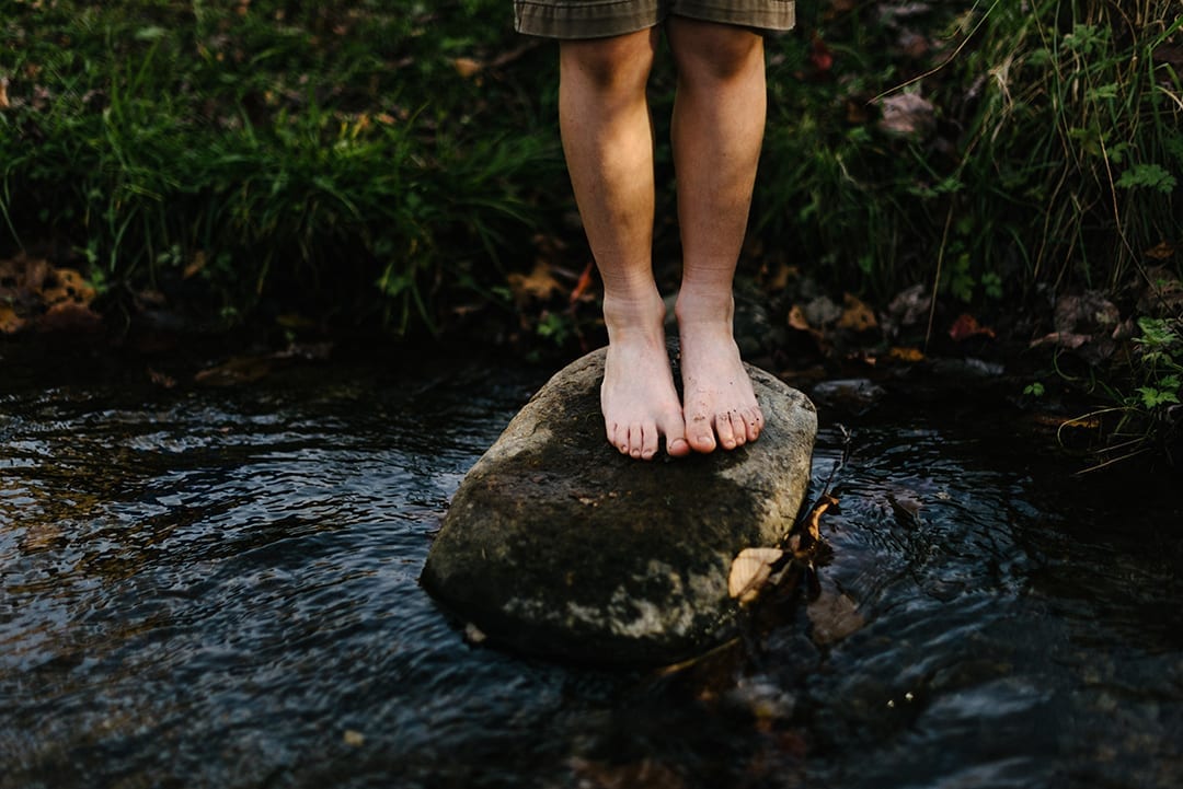 Un niño descalzo parado sobre una roca en un arroyo