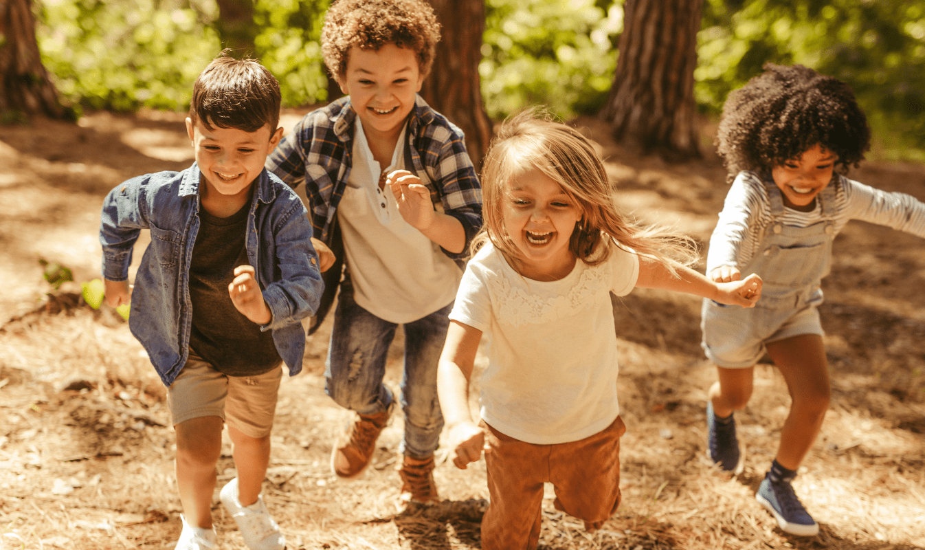 Un grupo de cuatro niños  corren y ríen en un bosque